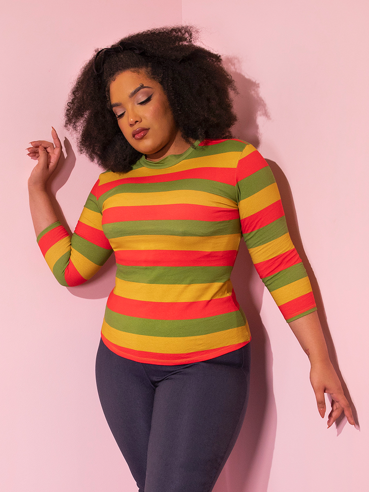 The Bad Girl 3/4 Sleeve Top in Orange/Yellow/Avocado Stripes being worn tucked out of tight-fitting pants.
