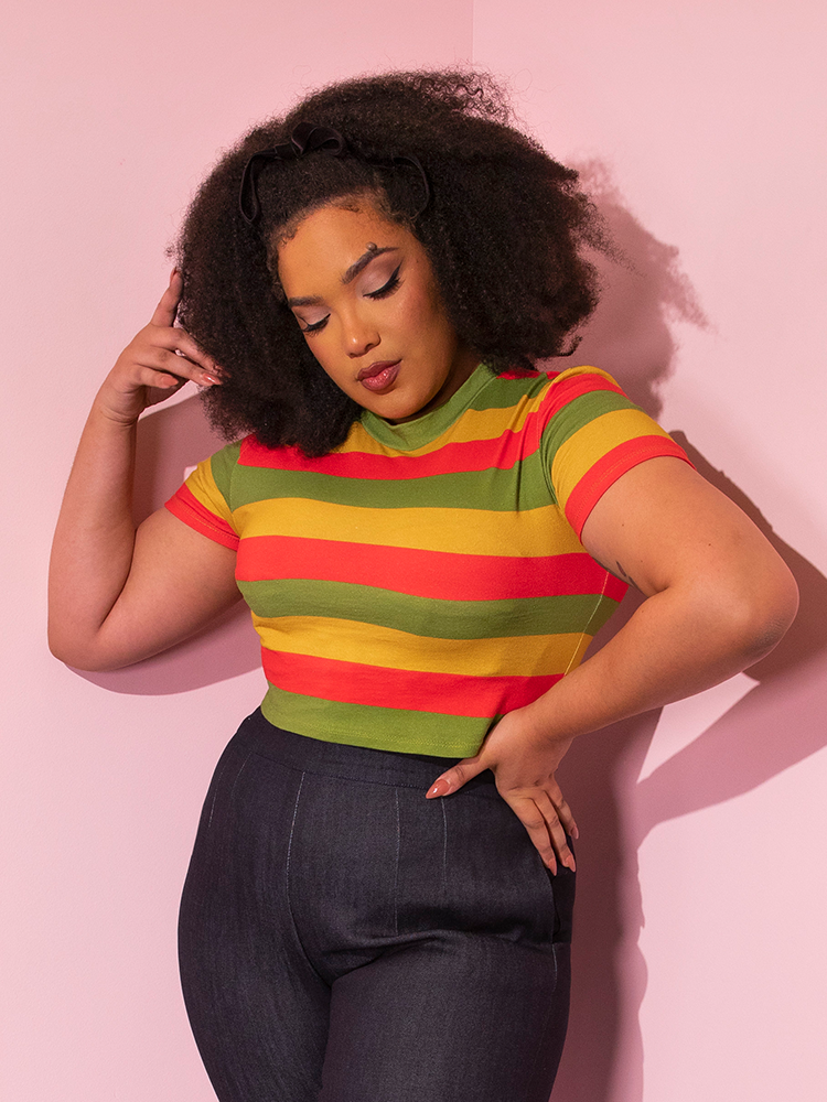 Model poses contemplatively while wearing the Bad Girl Crop Top in Orange/Yellow/Avocado Stripes tucked into dark denim.