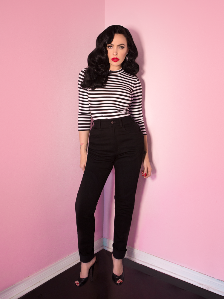 A full length shot of Micheline Pitt looking directly at the camera modeling the Bad Girl top in black and white stripes paired with black retro jeans.