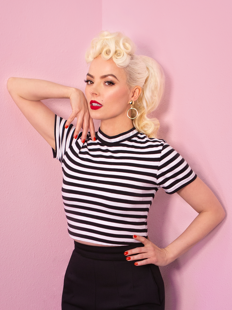 Seductively looking at the camera, Kelly Kathleen models the Bad Girl Crop Top in Black and White Stripes from vintage brand Vixen Clothing.
