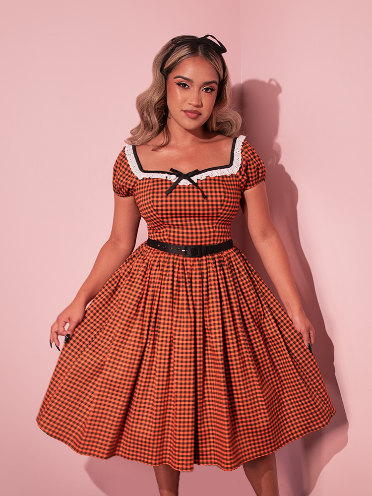 Embrace autumnal elegance with this vintage-inspired swing dress in orange pumpkin gingham, reminiscent of classic Hollywood style.