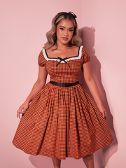 Embrace autumnal elegance with this vintage-inspired swing dress in orange pumpkin gingham, reminiscent of classic Hollywood style.