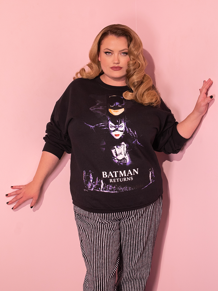 Blonde model wearing the BATMAN RETURNS™ Movie Poster Sweatshirt with black and white striped pants.