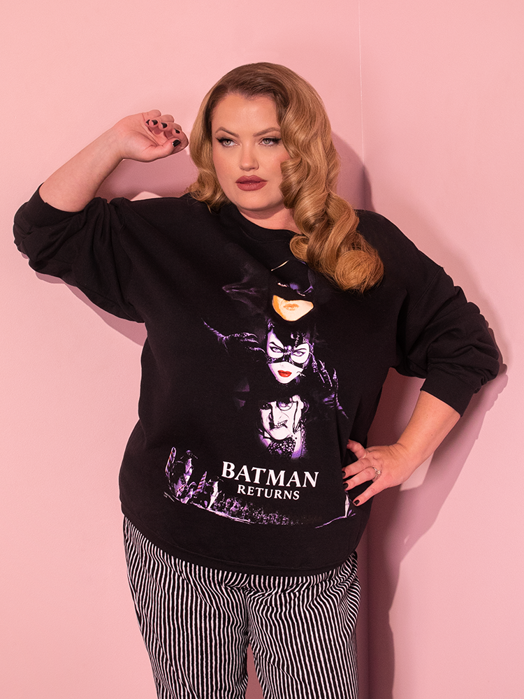 In a delightful display, the attractive dirty blonde-haired model playfully poses in the BATMAN RETURNS™ Movie Poster Sweatshirt (unisex) from the distinguished retro clothing brand Vixen Clothing.