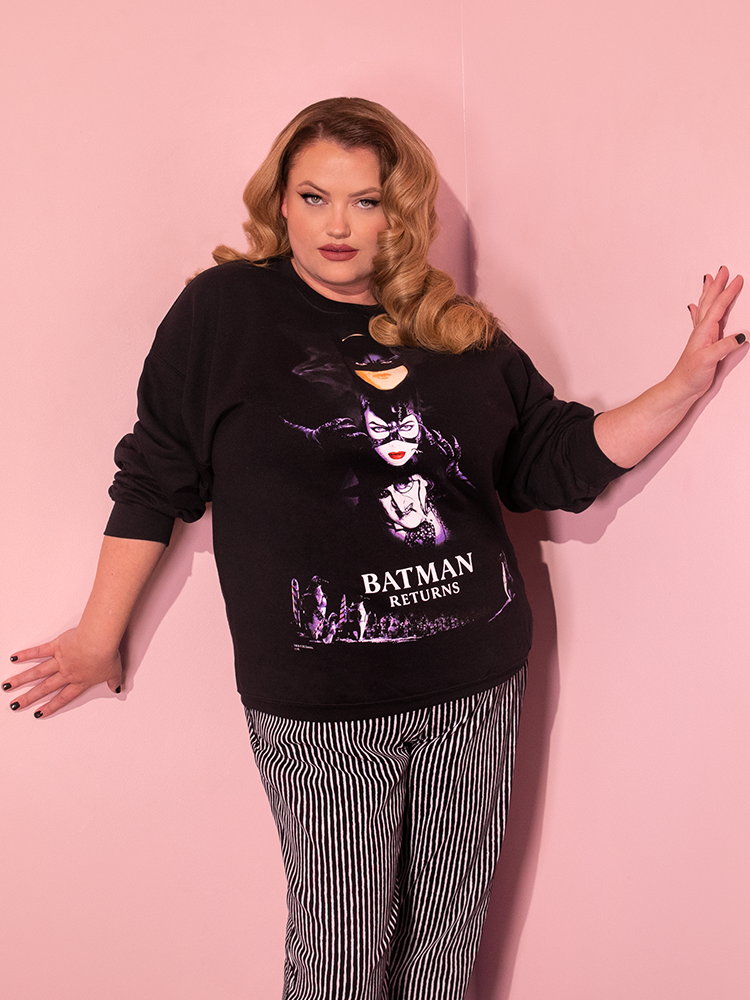 Capturing a moment of playfulness, the BATMAN RETURNS™ Movie Poster Sweatshirt (unisex) from Vixen Clothing graces the figure of an attractive dirty blonde-haired model.