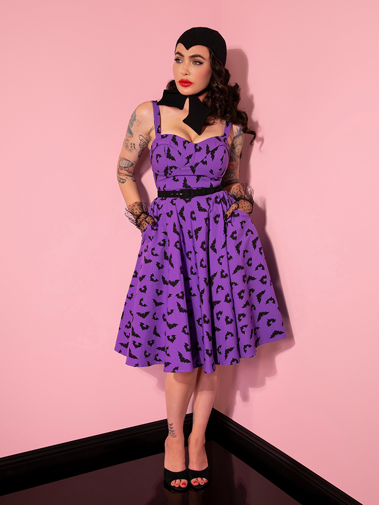 Micheline Pitt tucking her hands into the pockets of the Maneater Swing Dress in Bat Print from Vixen Clothing.