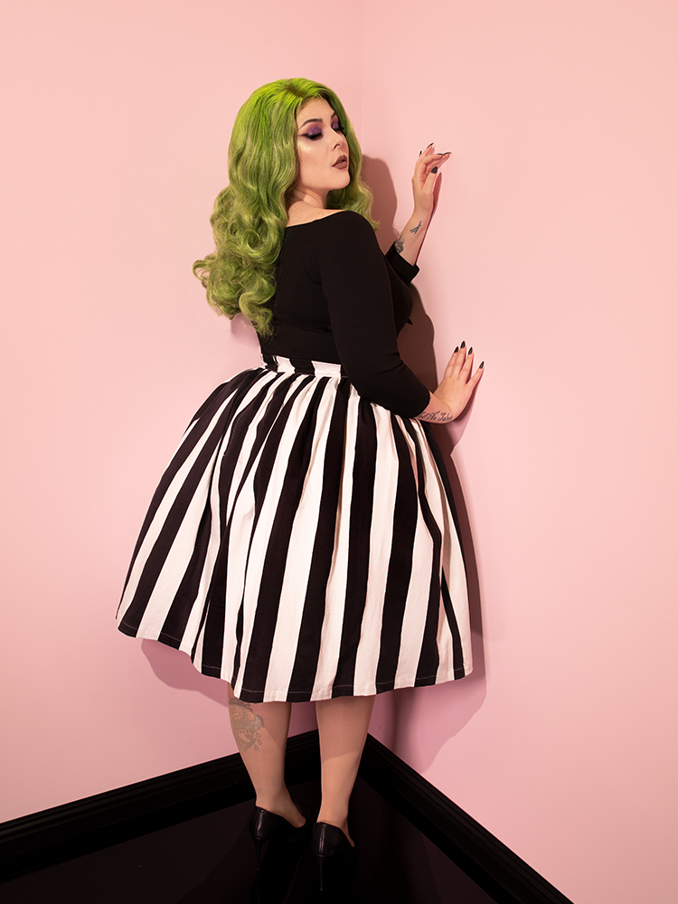 Green-haired model facing away from the camera to show off the back of her outfit inspired by Beetlejuice. Model wearing Ghost Swing Skirt in Black & White Stripes with black retro top.