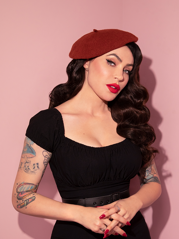 Waist level shot of Micheline Pitt standing in a black retro top and the all-new Vintage Style Beret in Rust. All items from vintage style clothing brand Vixen Clothing.