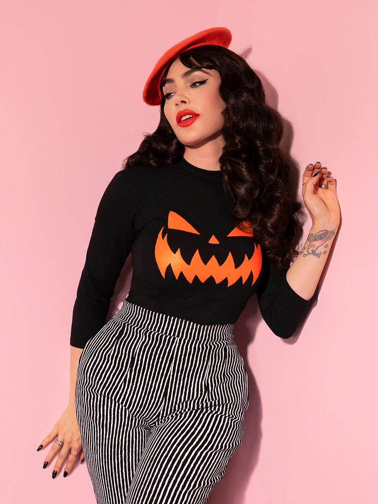 The Pumpkin King 3/4 Sleeve Top in Black and Orange being worn by Micheline Pitt and paired with an orange beret and black and white striped pants.