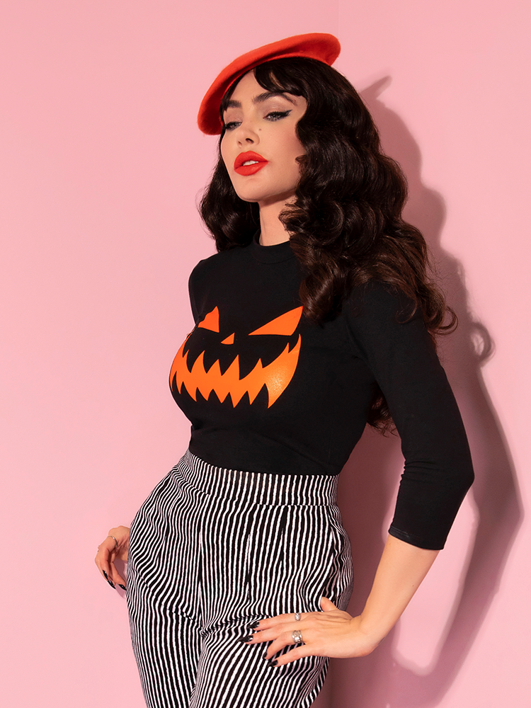 Micheline Pitt turned to the side and staring off camera in the Pumpkin King 3/4 Sleeve Top in Black and Orange from retro clothing brand Vixen Clothing.