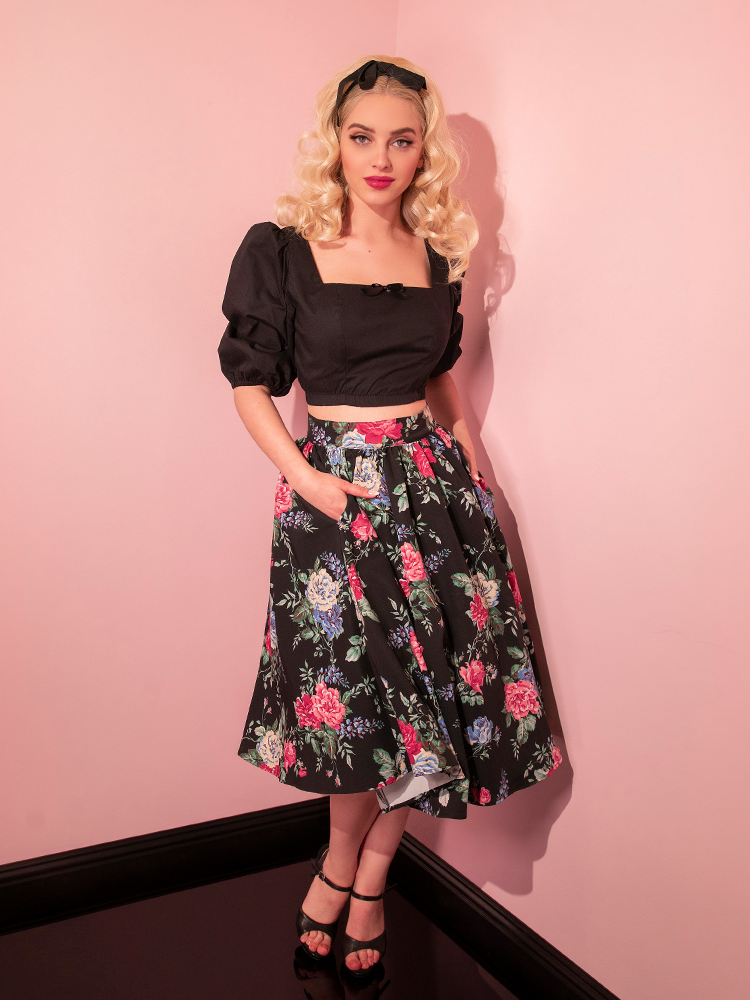 Model shows off the side pockets on the Vacation Swing Skirt in Black Rose Print from Vixen Clothing.