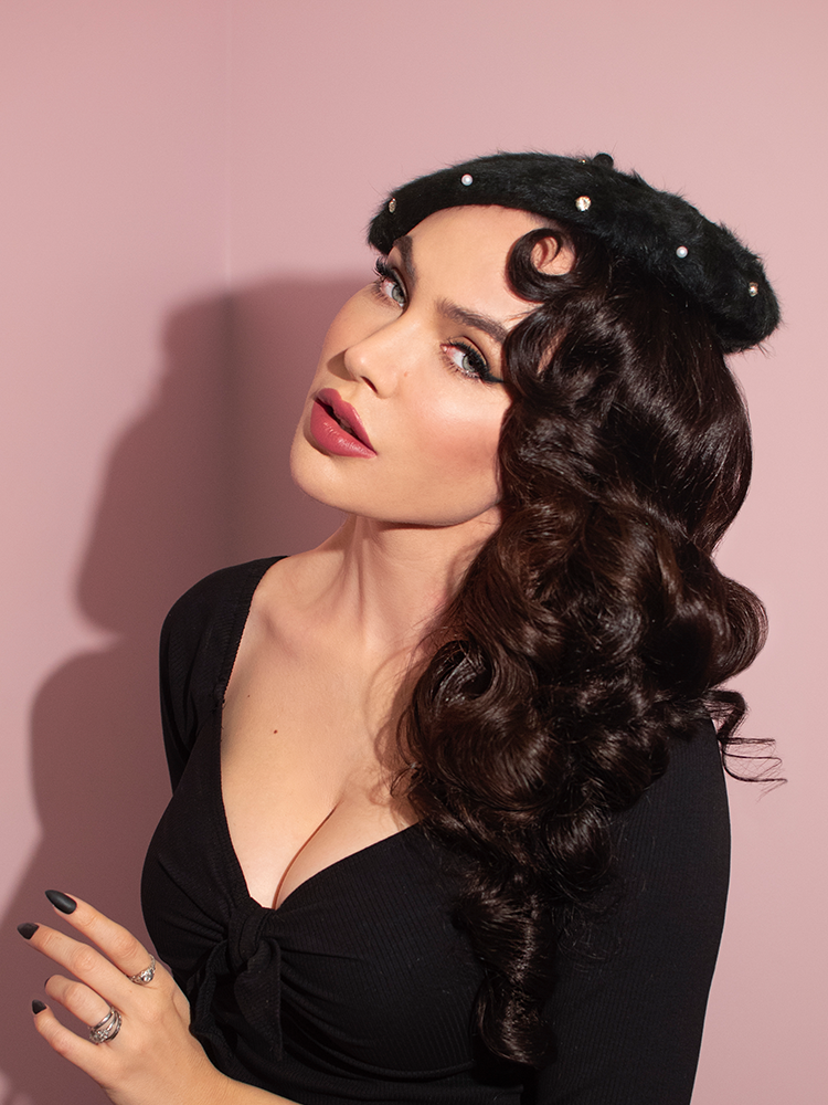 Micheline Pitt sits close to the camera and gazes directly into it while modeling the Vintage Style Beret with Rhinestones in Black.
