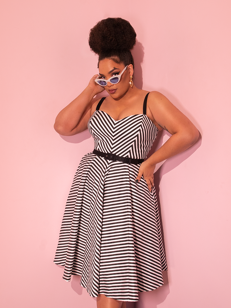 Model posing in the Dollface Dress in Black and White with matching sunglasses from the same line offered by retro clothing brand Vixen Clothing.