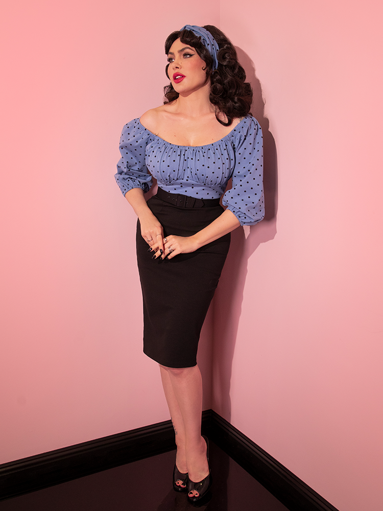 Full length shot of Micheline slightly bent forward and clasping her hands while wearing the Daydream Wiggle Dress in Sunset Blue Polka Dot.
