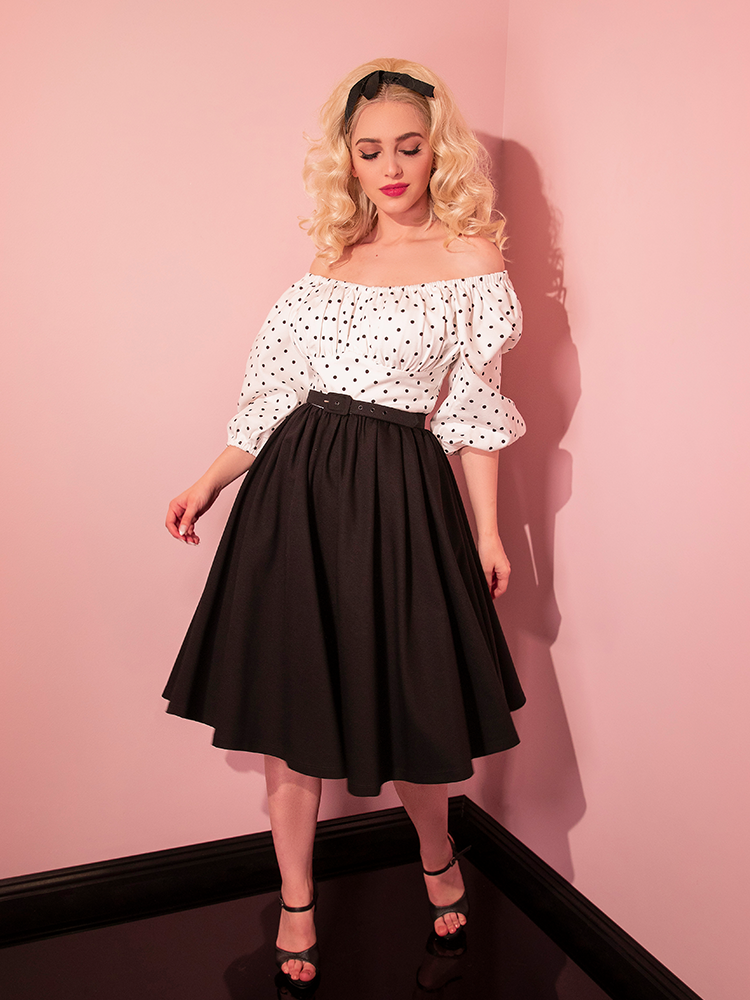 Sofia poses seductively in the corner of her pink room while wearing the Daydream Swing Dress in Black Polka Dot.