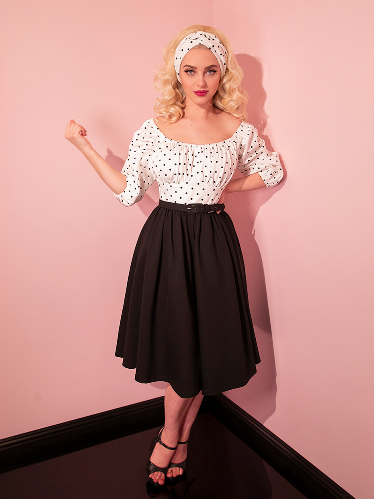 Full length shot of Sofia wearing the Daydream Swing Dress in Black Polka Dot with matching headband - all items available from Vixen Clothing.