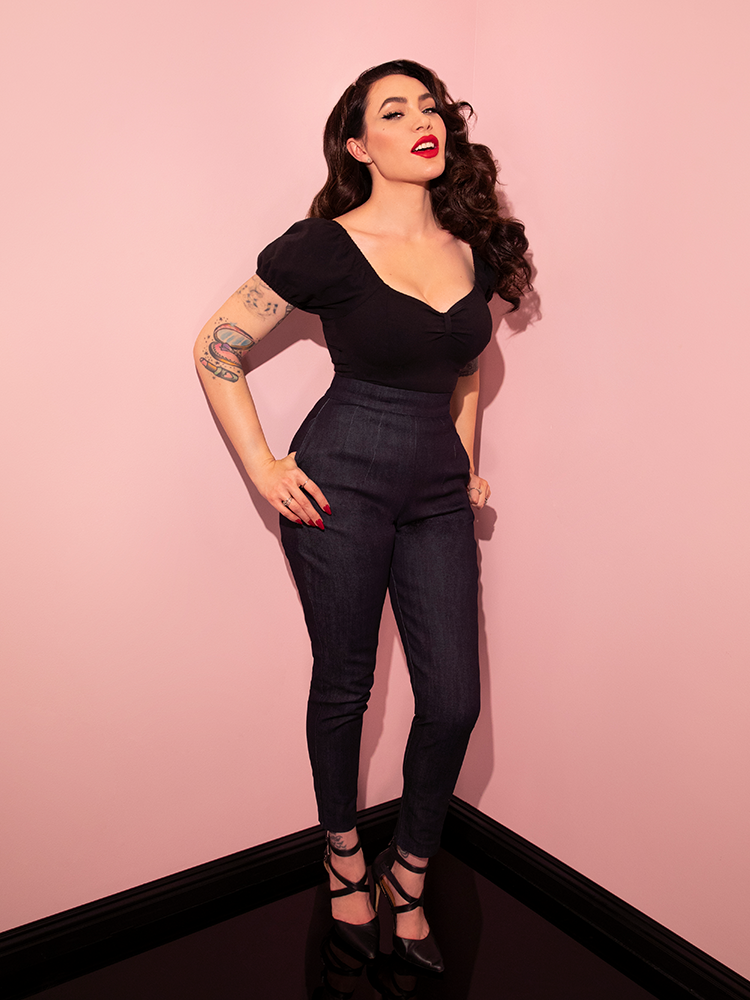 The Cigarette Pants in Denim being worn by Micheline Pitt with a low-cut black top tucked into them