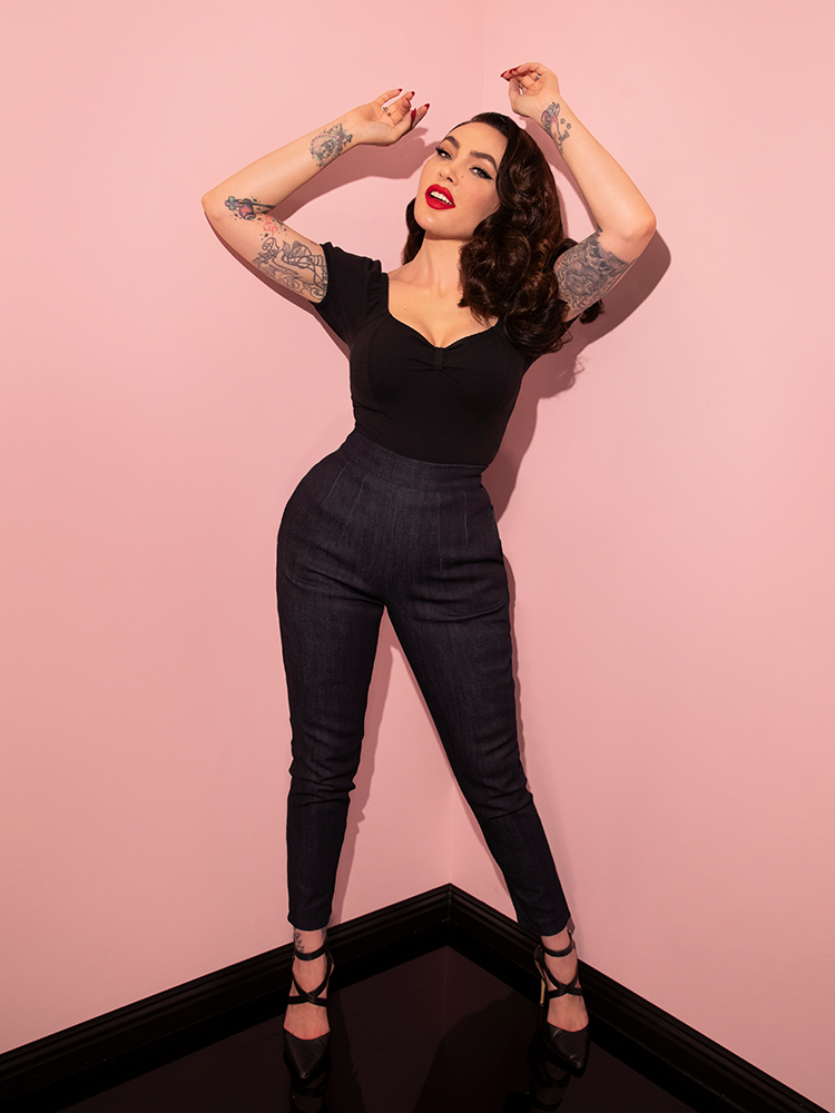 Micheline Pitt playfully posing in the Cigarette Pants in Denim with a low-cut black top to show off the ultimate retro outfit.