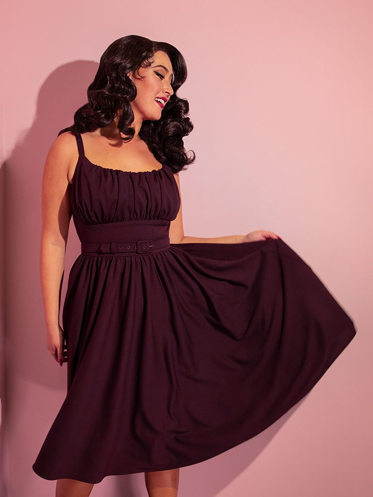 Model smiles while tossing the skirt section of her Ingenue Swing Dress in Eggplant Purple out to show off the gorgeous color.