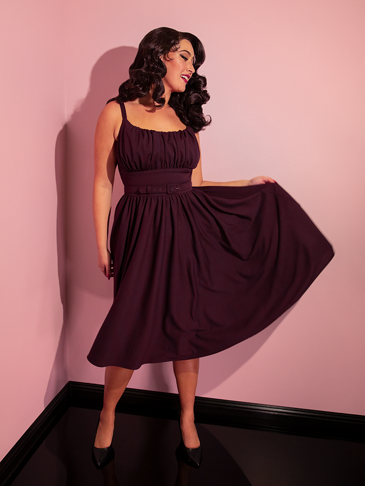 Brittany smiles as she shows off the skirt section of the Ingenue Swing Dress in Eggplant Purple from retro dress company Vixen Clothing.