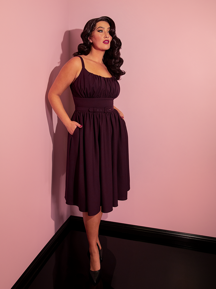 Full length shot of Brittany tucking her hands into the pockets of her Ingenue Swing Dress in Eggplant Purple.