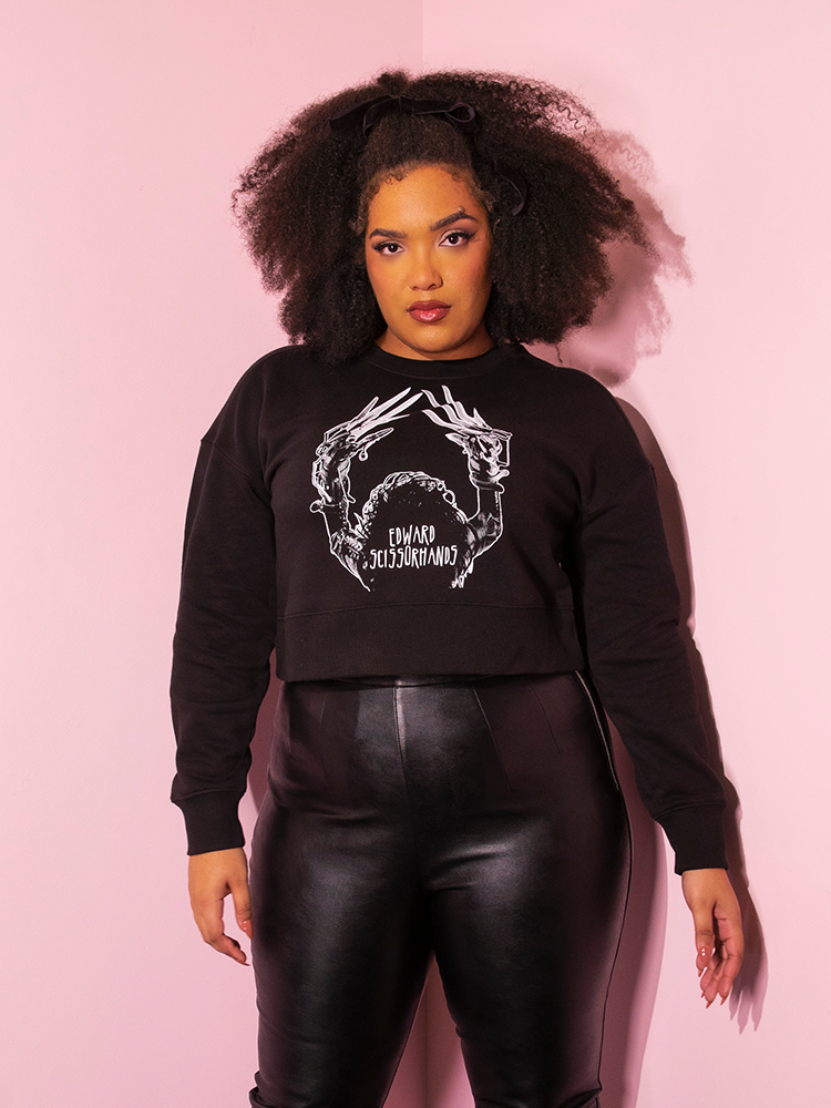 Female model wearing an all black retro outfit featuring the all-new EDWARD SCISSORHANDS Graphic Cropped Sweatshirt in Black from Vixen Clothing.