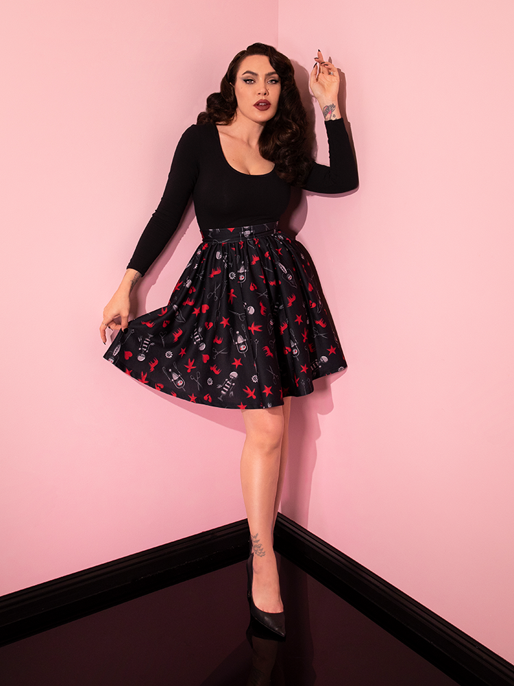 Full length shot of Micheline Pitt posing in the EDWARD SCISSORHANDS Skater Skirt in “I am not complete” Novelty Print with retro style black top and black heels.