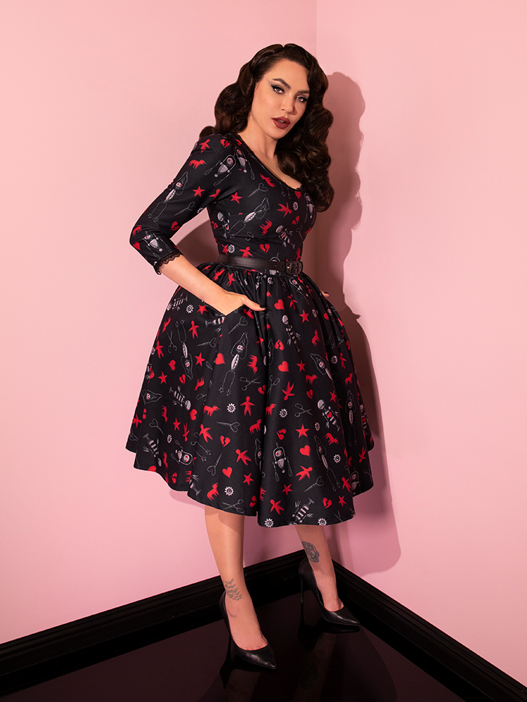 Profile shot of Micheline Pitt posing in the EDWARD SCISSORHANDS Storytime Swing Dress in “I am not complete” Novelty Print with her hands tucked into the pockets.