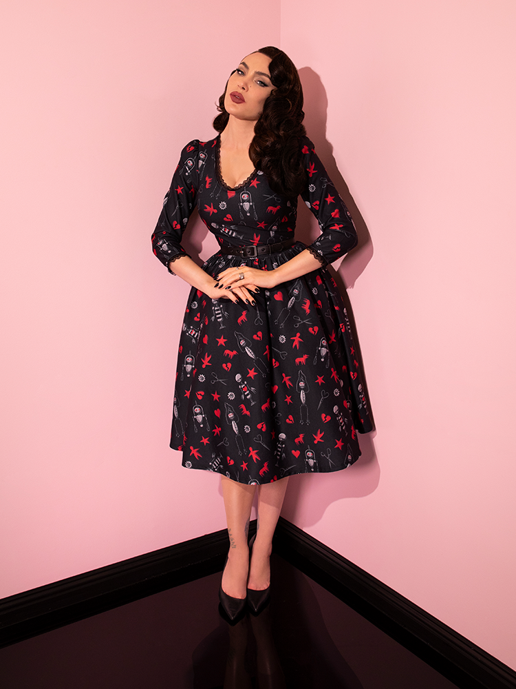 Micheline Pitt posing with her hands clasped in front of her while wearing the EDWARD SCISSORHANDS Storytime Swing Dress in “I am not complete” Novelty Print from vintage dress company Vixen Clothing.