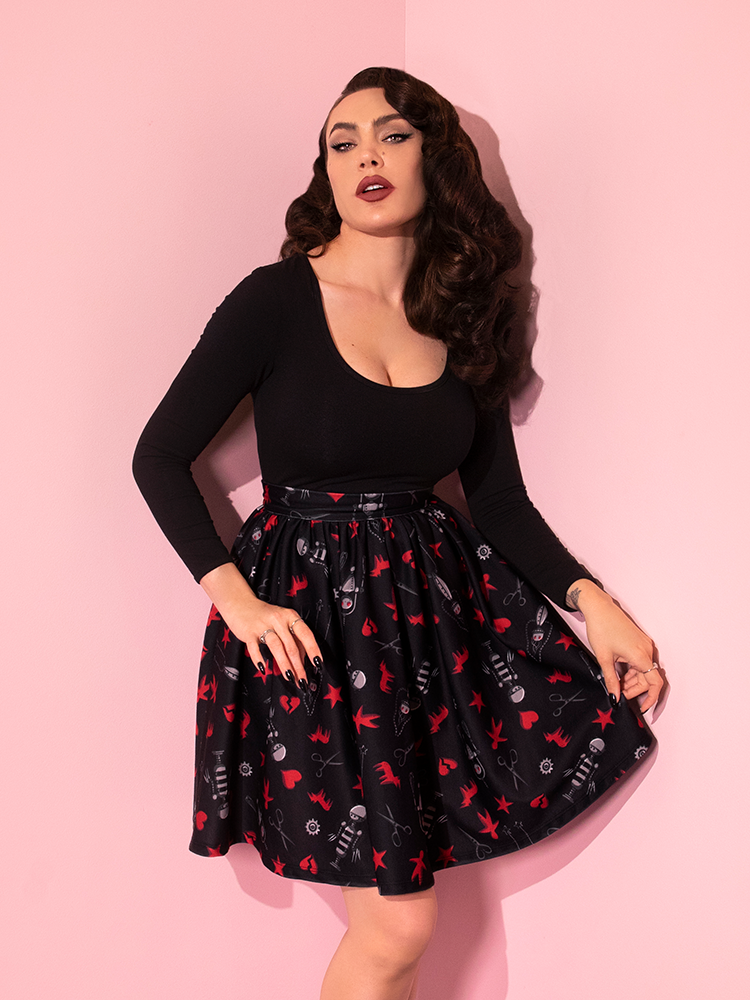 Micheline Pitt posing in the EDWARD SCISSORHANDS Skater Skirt in “I am not complete” Novelty Print and gently pulling on the skirt to show off the intricate gothic design elements.