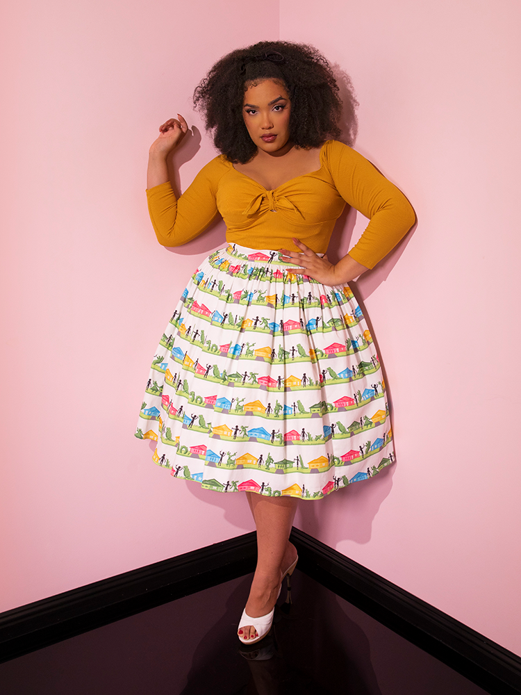 Model posing in the corner of a pink showroom while wearing the EDWARD SCISSORHANDS Swing Skirt in Suburban Topiary Novelty Print with mustard colored retro style top.