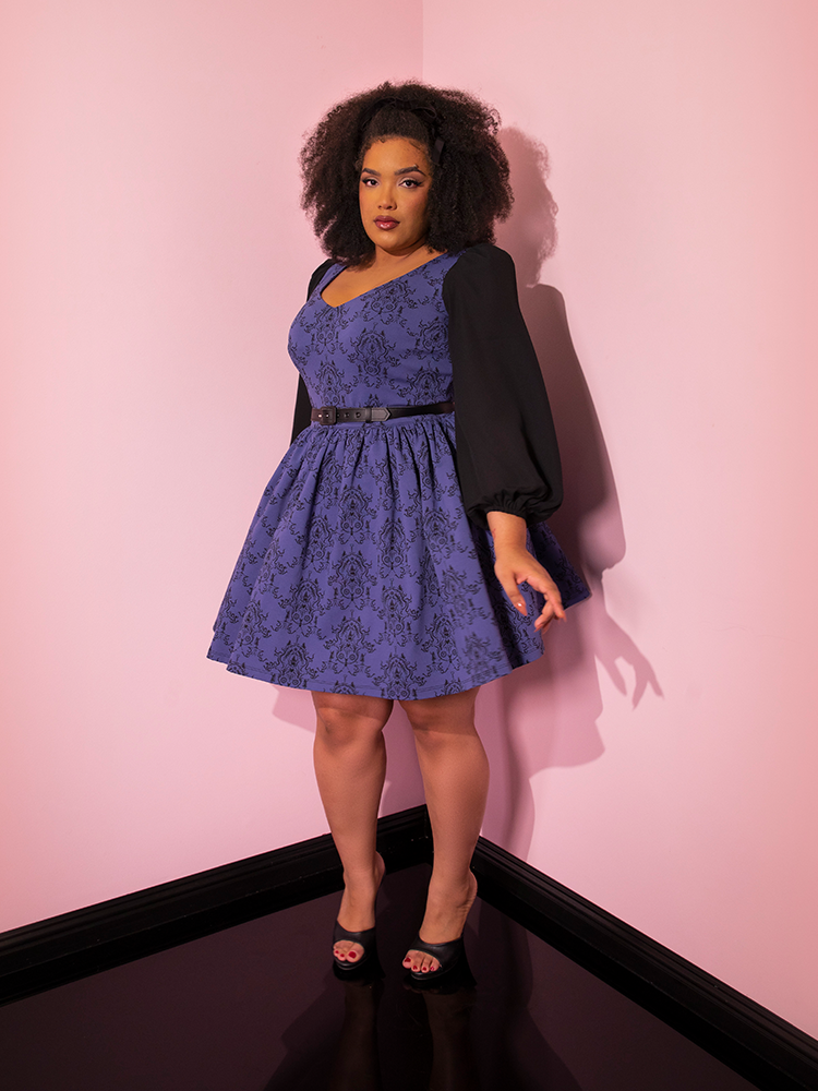 Model posing with on hand pointing out towards the wall while wearing the EDWARD SCISSORHANDS Farewell Babydoll Dress in Wallpaper Novelty Print.