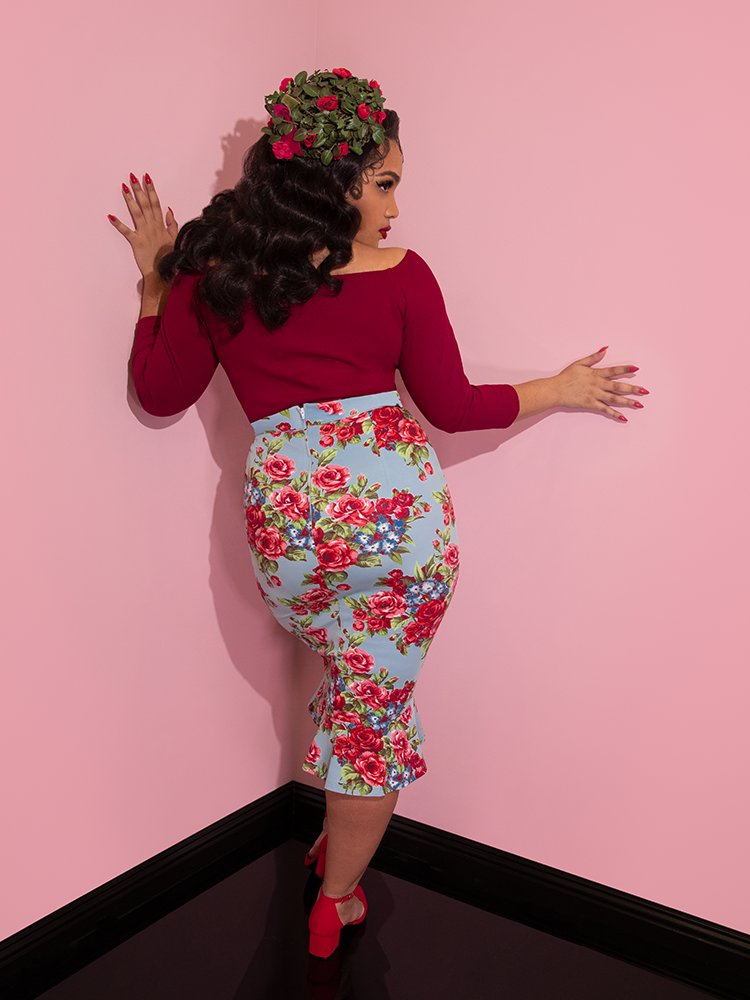 A back view of Ashleeta wearing a floral hat modeling the Vixen flutter skirt in blue and red rose print paired with a red tie up top.
