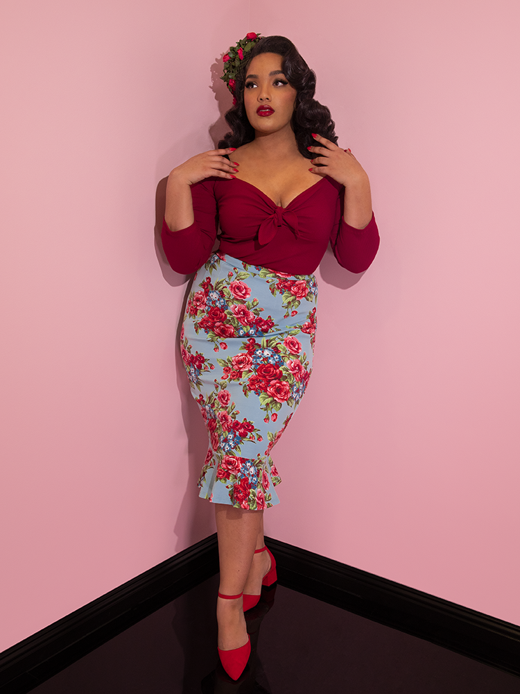 Ashleeta wearing a floral hat modeling the Vixen flutter skirt in blue and red rose print paired with a red tie up top.