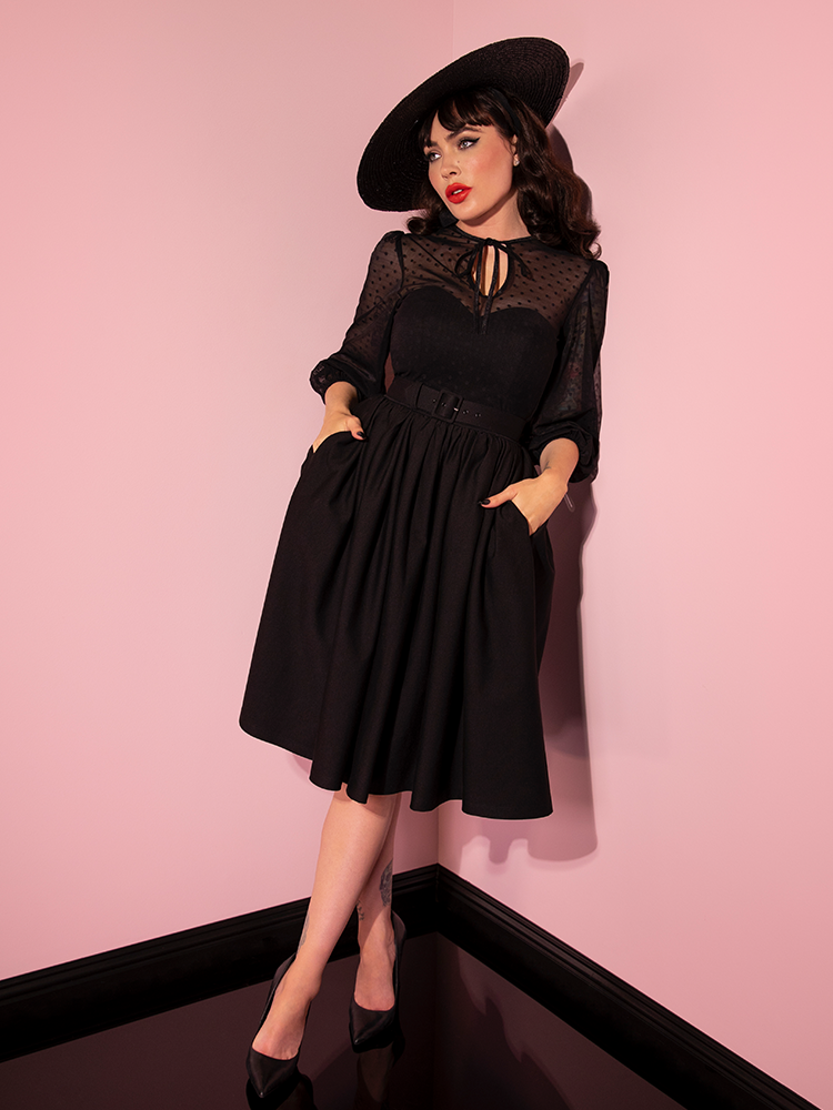 Micheline Pitt with her hands tucked into the pockets of her Frenchie Swing Dress in Black.