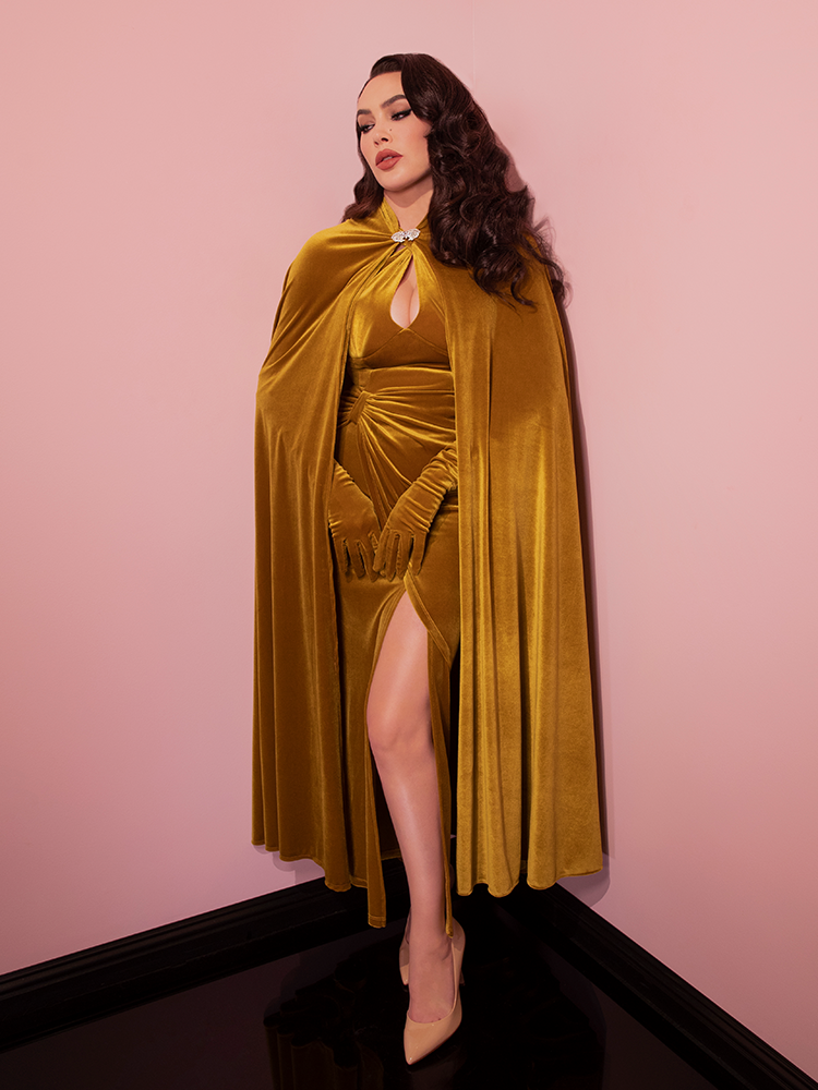 The Golden Era Cape in Gold Velvet from Vixen Clothing paired with matching retro style dress, elbow length gloves and matching color heels.