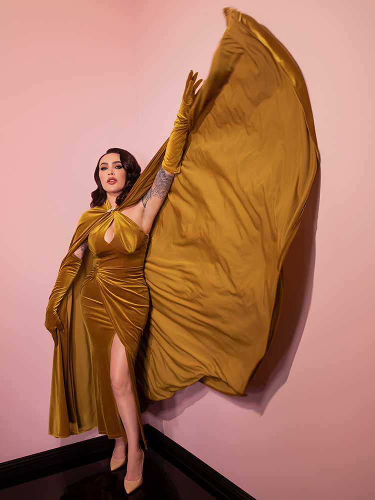 Micheline is elegantly throwing her cape in a pink room while wearing the Golden Era gown and glove set.