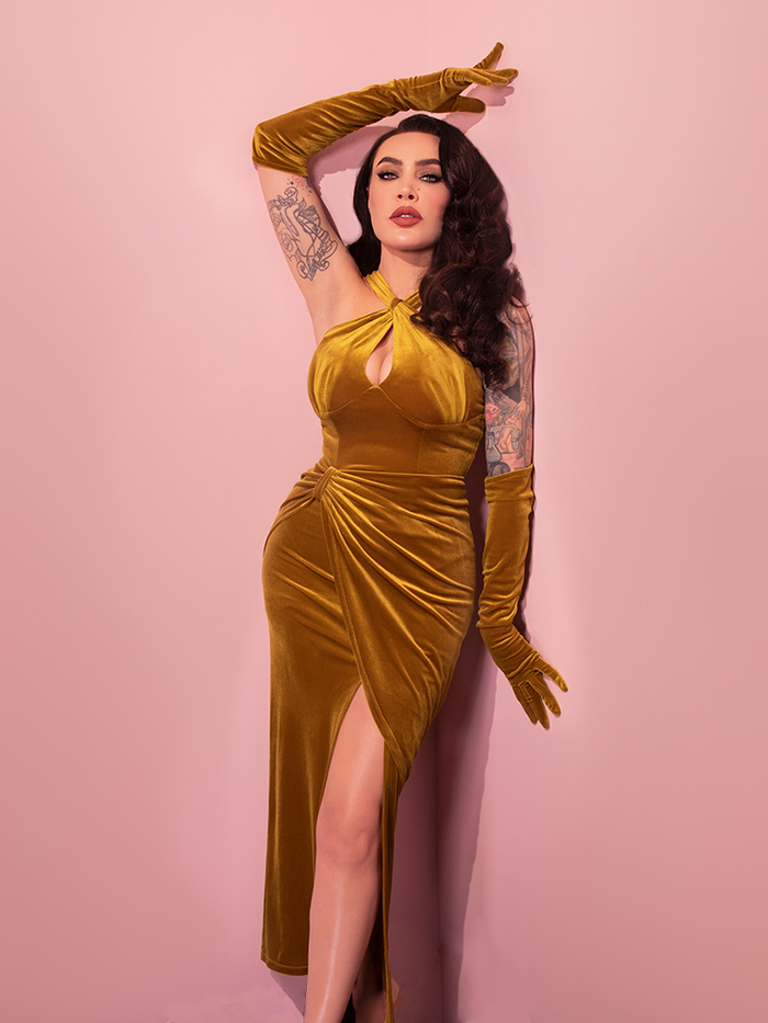 Micheline is leaning against a pink wall with her arm above her head wearing the Golden Era gown and glove set.