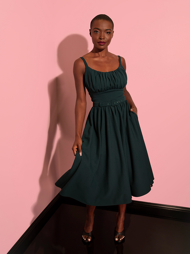 Full length shot of model gently swinging the skirt on her Ingenue Dress in Hunter Green from Vixen Clothing.