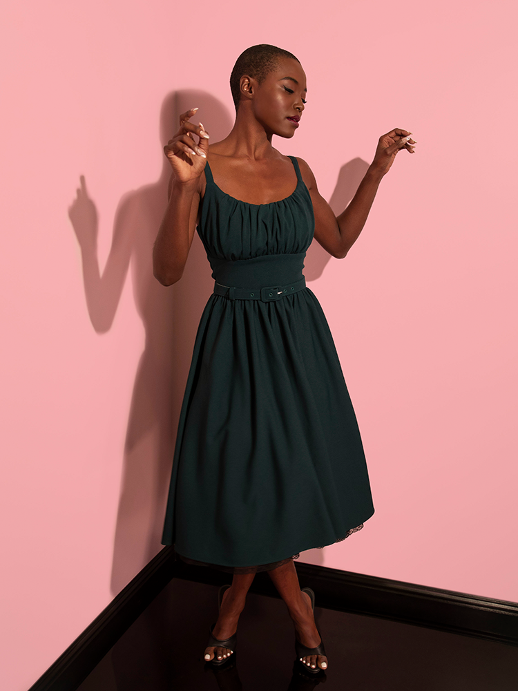 Model posing with her arms slightly held upwards and closing her eyes while wearing the Ingenue Dress in Hunter Green.