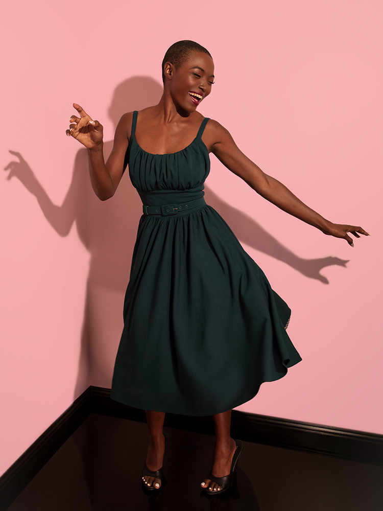 Laughing and dancing, model wears a retro style dress in hunter green color from vintage inspired clothing company Vixen Clothing.