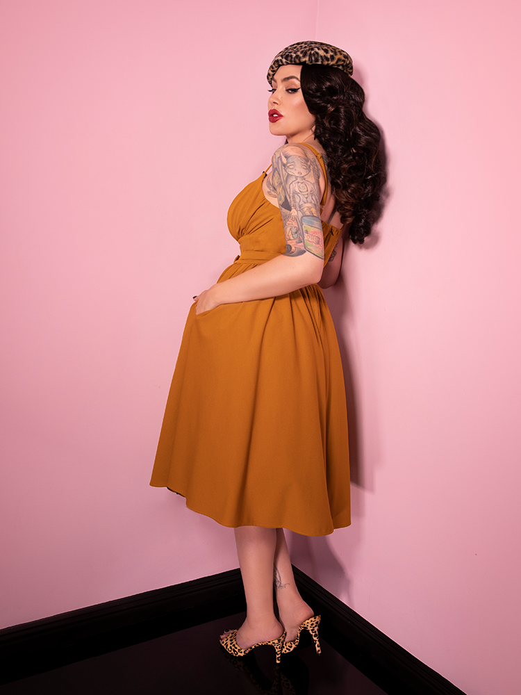 With her body facing away from the camera and looking back alluringly at the camera, Micheline Pitt shows off the Ingenue Dress in Vintage Mustard Print.