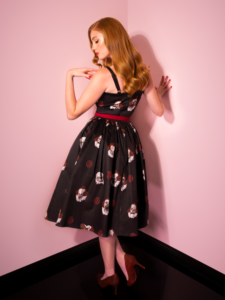 Turned away from the camera and looking down, Emily models the back of the Pennywise sweetheart swing dress by Vixen Clothing.