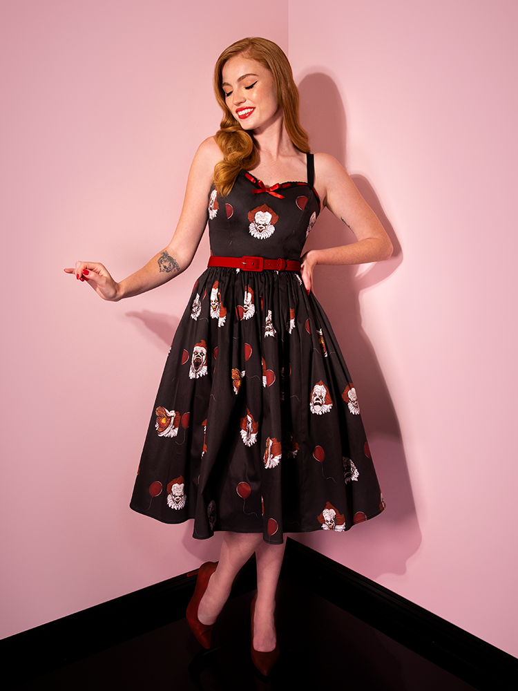 Looking down with her hand on her hip, Emily shows off the Pennywise sweetheart swing dress by Vixen Clothing.