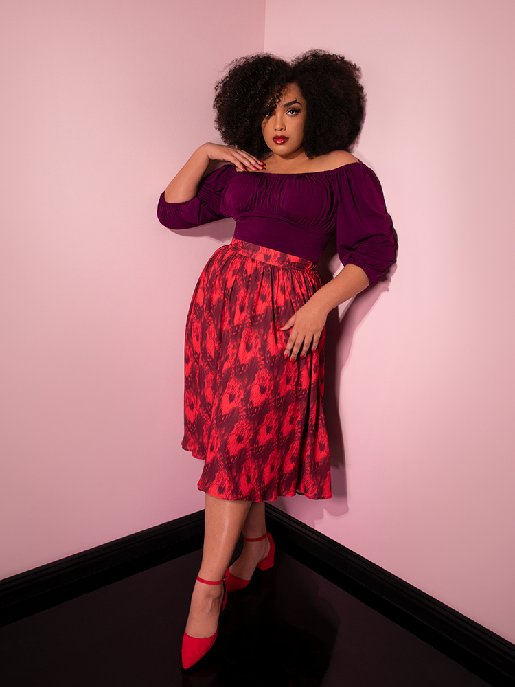 With her hand on her shoulder while leaning against a pink wall, Ashleeta models the Pennywise cottage skirt by Vixen Clothing.