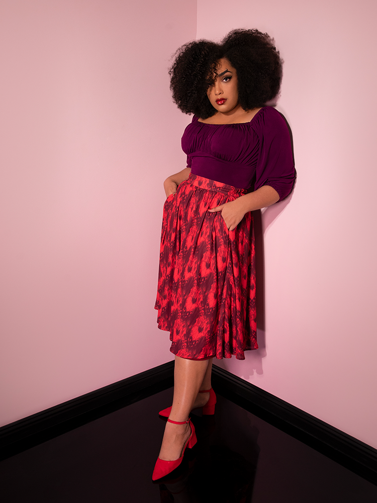Leaning against a pink wall with her hands in her pockets, Ashleeta models the Pennywise cottage skirt by Vixen Clothing.