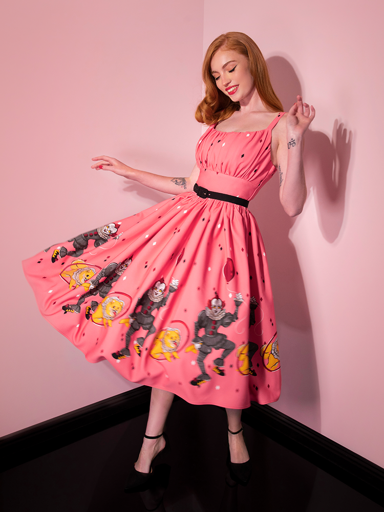 Twirling around with her hands in the air, Emily models the Dancing Clown Ingenue swing dress in pink by Vixen Clothing.