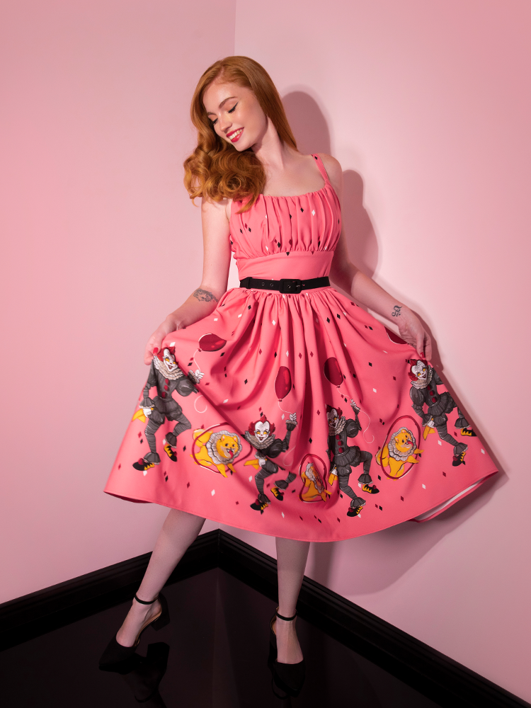 Fanning the skirt out with her hands, Emily models the Dancing Clown Ingenue swing dress in pink by Vixen Clothing.