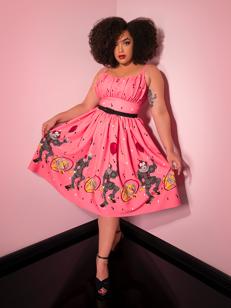 Fanning out the skirt with her hands, Ashleeta models the Dancing Clown Ingenue swing dress in pink by Vixen Clothing.