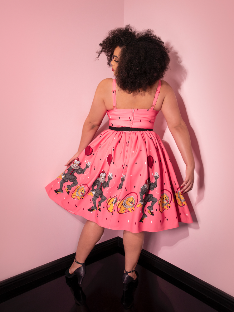 Turned away from the camera, Ashleeta models the back of the Dancing Clown Ingenue swing dress in pink by Vixen Clothing.